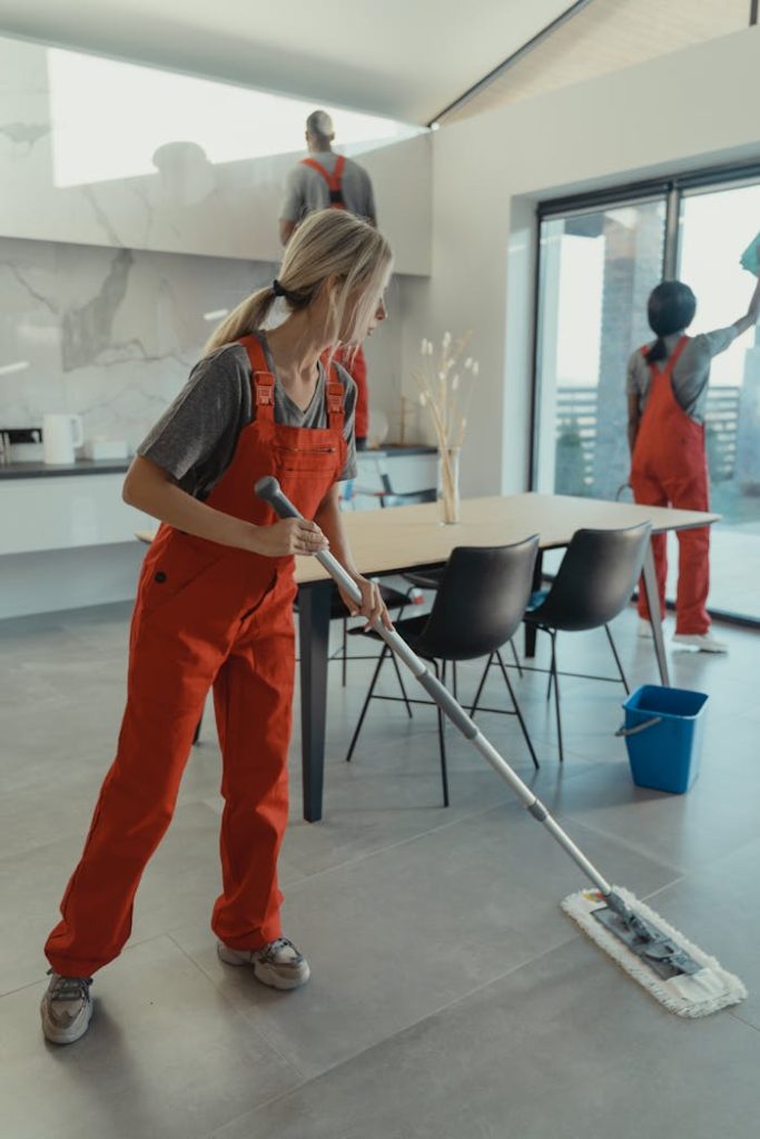 woman-holding-a-mop-6197116 Cleaning team in red overalls mopping and sanitizing a modern home interior.